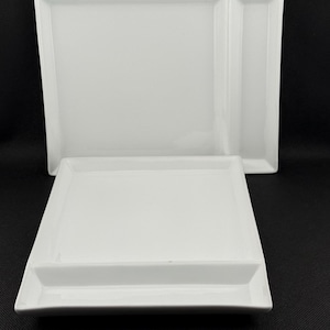 May include: Two white rectangular serving platters. One platter has a rectangular section on the side. The platters are made of a glossy white material and are set against a black background.