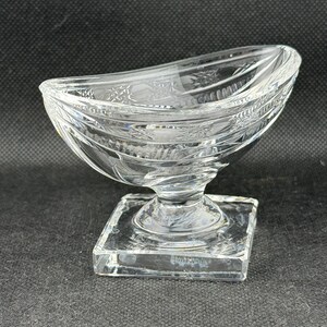 May include: A clear, decorative glass bowl with a square base and a curved, boat-like top. The bowl features etched floral and geometric patterns. The glass is transparent, allowing light to pass through, and is suitable for serving or display.