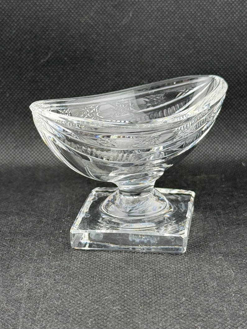May include: A clear, decorative glass bowl with a square base and a curved, boat-like top. The bowl features etched floral and geometric patterns. The glass is transparent, allowing light to pass through, and is suitable for serving or display.
