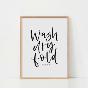 Puede incluir: Una impresión enmarcada con caligrafía negra que dice "Wash dry fold repeat" sobre un fondo blanco.