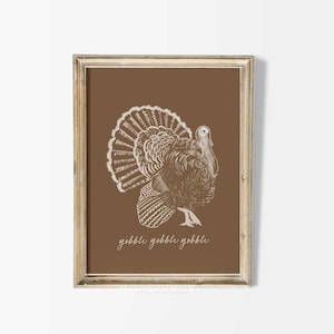 May include: A brown framed print with a white illustration of a turkey with the text "gobble gobble gobble" underneath.