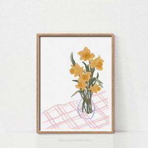 Puede incluir: Una impresión enmarcada de un bodegón con un ramo de narcisos amarillos en un jarrón de vidrio transparente sobre un mantel a cuadros rosa y blanco.