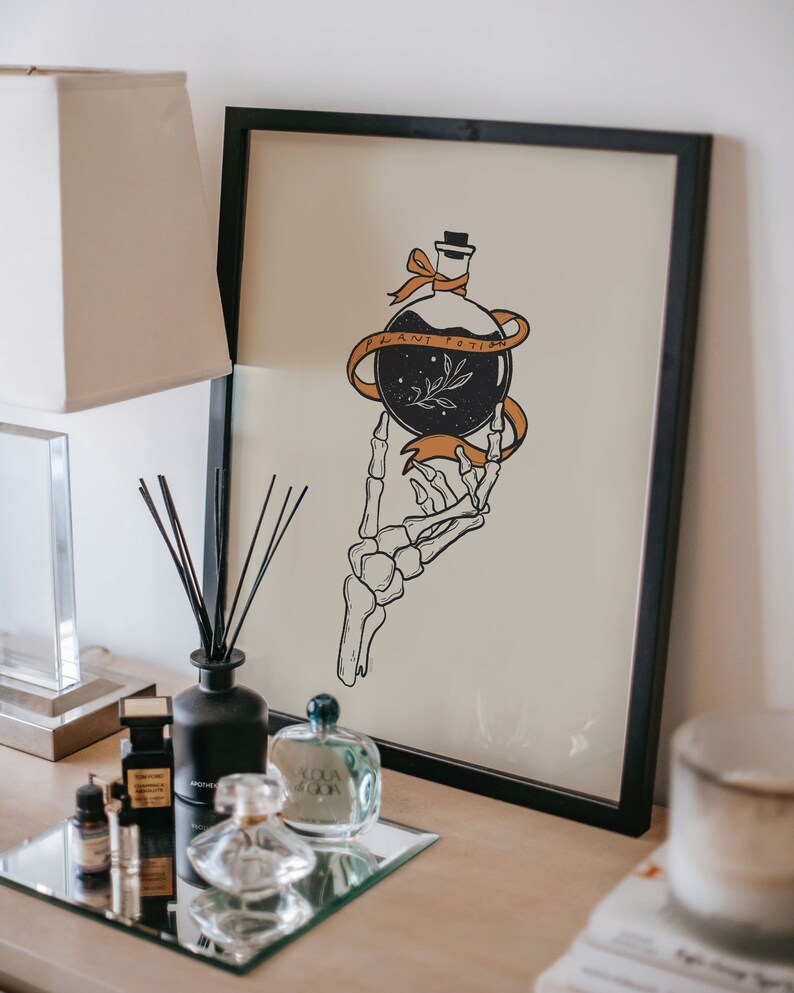 May include: Black and white illustration of a skeletal hand holding a bottle with a ribbon that says "Plant Potion". The illustration is on a beige background and framed in black.