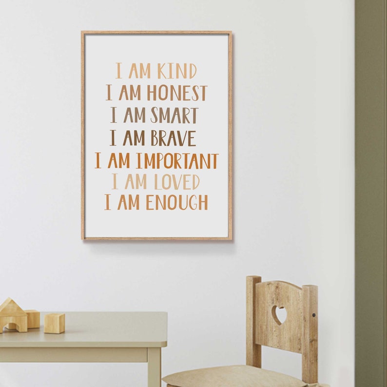 May include: A framed print with the words "I AM KIND, I AM HONEST, I AM SMART, I AM BRAVE, I AM IMPORTANT, I AM LOVED, I AM ENOUGH" in various shades of brown. The print is in a light wood frame and hangs on a white wall.
