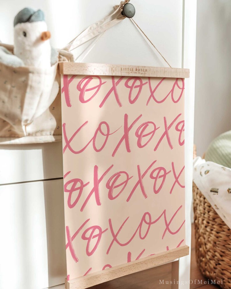 Puede incluir: Una impresi&oacute;n rosa y blanca con la palabra "XOXO" repetida en una fuente de pinceladas. La impresi&oacute;n est&aacute; enmarcada en un marco de madera natural y colgada en una pared blanca.