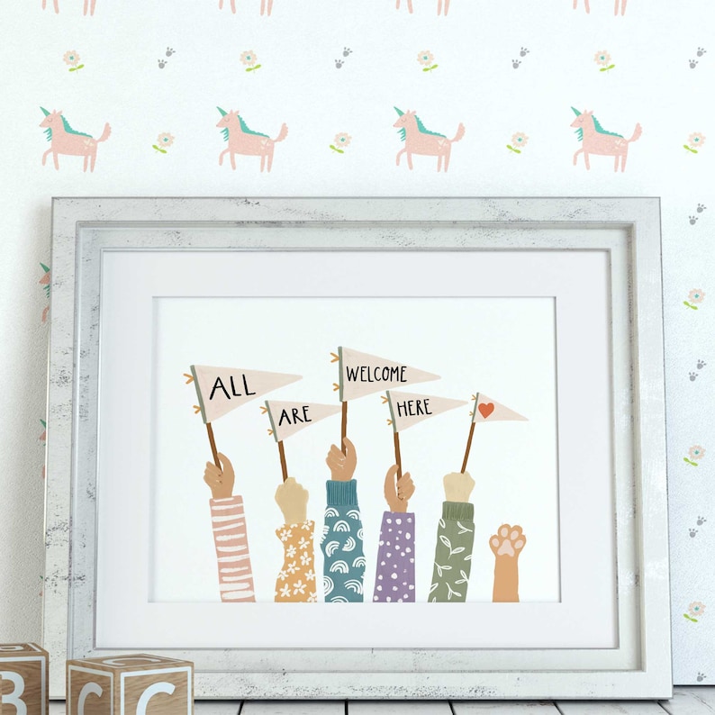 May include: Framed art print with the words "ALL ARE WELCOME HERE" on pennant flags held by diverse hands. The hands have various sleeve patterns. The background features a unicorn and floral pattern.