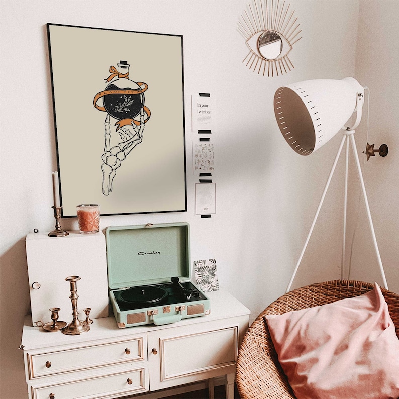 May include: A vintage-style record player with a light green exterior and a black turntable. The record player is sitting on a white dresser with a framed print of a skeleton hand holding a bottle with a label that reads "The Only Thing Worth Fighting For."
