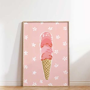 May include: A framed print featuring a whimsical illustration of a three-scoop ice cream cone. The ice cream is a gradient of pink hues, set against a pink background adorned with white floral accents. The cone is a golden brown color.