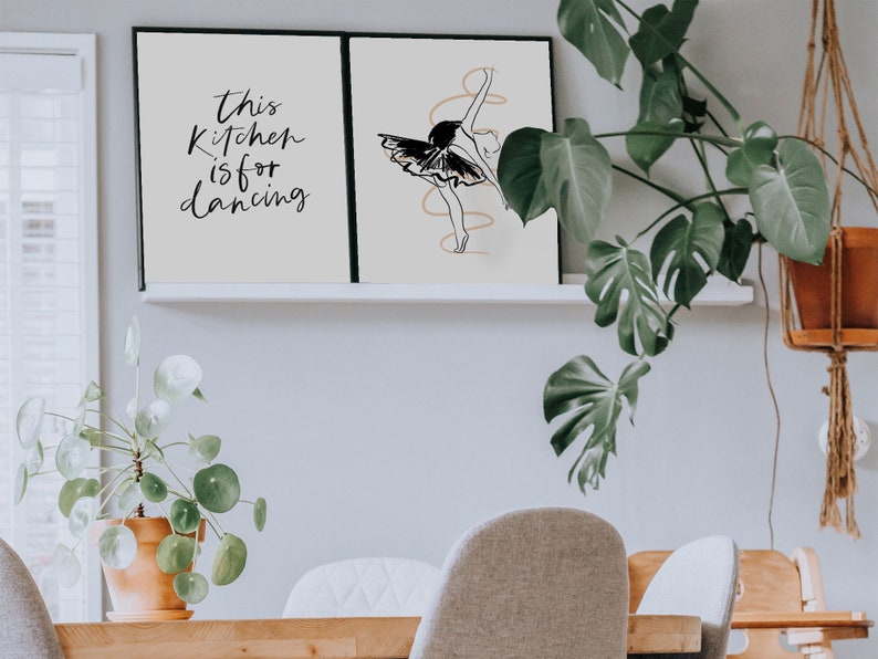 May include: Two framed prints on a white shelf. The print on the left says "This kitchen is for dancing". The print on the right features a black and white line drawing of a ballerina.