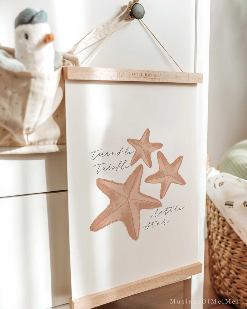 May include: A white framed print with a light brown background featuring three starfish and the text "Twinkle Twinkle Little Star". The print is hanging on a wall with a wooden dowel rod at the top and bottom.