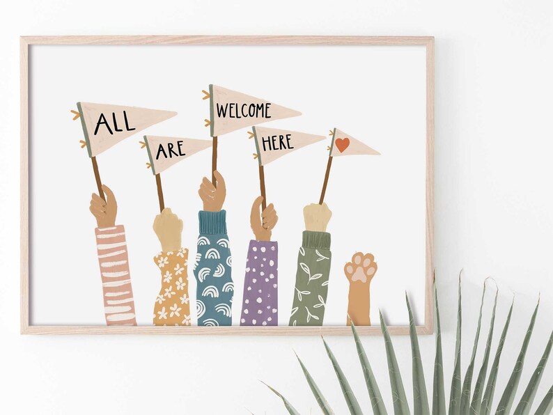 May include: A framed art print featuring hands holding pennant flags with the words "ALL ARE WELCOME HERE." The hands have various skin tones and patterned sleeves. One hand holds a paw print. The flags are beige with black text and a red heart.