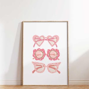 Puede incluir: Una impresión enmarcada con tres pares de gafas de sol rosas. Las gafas de sol tienen forma de corazón, flor y ojo de gato. La impresión tiene el texto "MusingsOfMeiMei" en la parte superior.