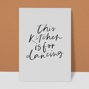 May include: A white card with black handwritten text that reads "This kitchen is for dancing".