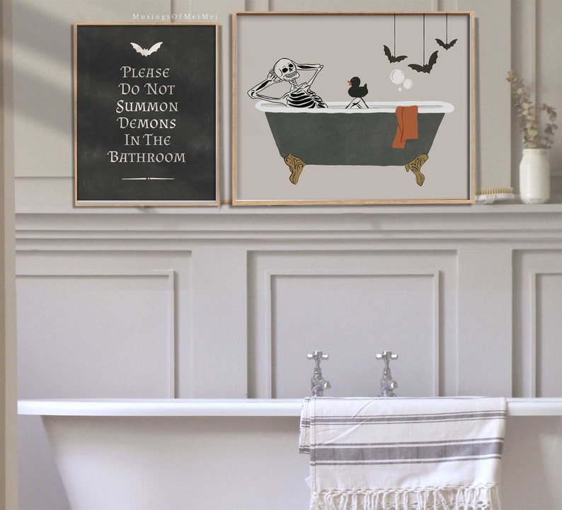 May include: Two framed prints with a Halloween theme. The first print is a black and white illustration of a skeleton taking a bath with a rubber ducky. The second print is a black chalkboard with the text "Please Do Not Summon Demons In The Bathroom".