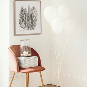 May include: A framed black and white drawing of a group of trees hangs on a white wall. A pink velvet chair with a stack of books sits in the corner of the room. Three white balloons are tied together with white ribbon and are floating in the corner of the room.