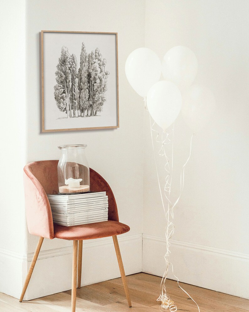 May include: A framed black and white drawing of a group of trees hangs on a white wall. A pink velvet chair with a stack of books sits in the corner of the room. Three white balloons are tied together with white ribbon and are floating in the corner of the room.