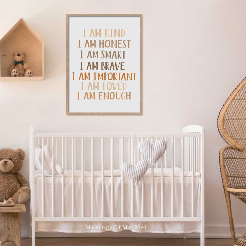 May include: A framed print with the words "I AM KIND, I AM HONEST, I AM SMART, I AM BRAVE, I AM IMPORTANT, I AM LOVED, I AM ENOUGH" in a copper color. The print is in a light wood frame and hangs above a white crib.