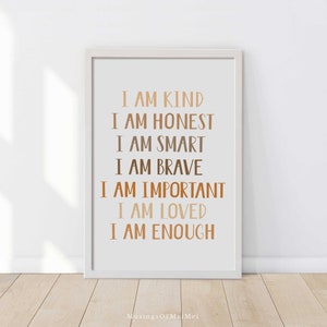 May include: A framed print with the words "I AM KIND, I AM HONEST, I AM SMART, I AM BRAVE, I AM IMPORTANT, I AM LOVED, I AM ENOUGH" in various shades of brown. The print is in a white frame and is displayed against a white wall.