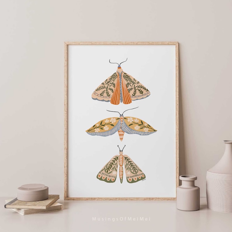 Wall art with 3 Soft pastel colored moth and butterflies arranged vertically. Butterflies have floral and botanical patterns on them. Colors on butterflies include sage green, pastel yellow, dusty blue, light coral,blush pink on a white background.