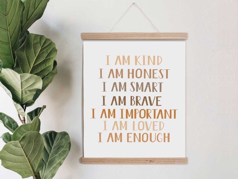 May include: A motivational art print with the words "I AM KIND, HONEST, SMART, BRAVE, IMPORTANT, LOVED, ENOUGH" in brown and tan lettering. The print is displayed on a white background and held by a wooden frame, with a hanging string.