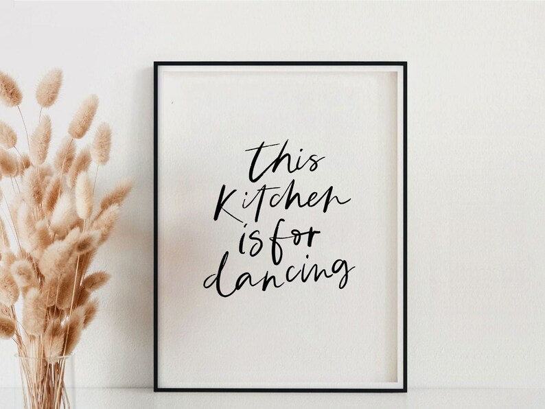 May include: A black framed print with white background and black text that reads "This kitchen is for dancing".