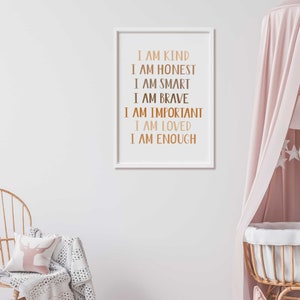 May include: A framed print with the words "I AM KIND, I AM HONEST, I AM SMART, I AM BRAVE, I AM IMPORTANT, I AM LOVED, I AM ENOUGH" in a copper color. The print is in a white frame, hanging on a white wall.