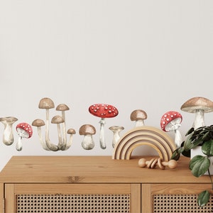 May include: A wall decal featuring a cluster of brown and white mushrooms with red tops. The mushrooms are arranged in a row along the bottom of the image. The decal is placed above a wooden table with a rainbow-colored wooden arch and a wooden toy.