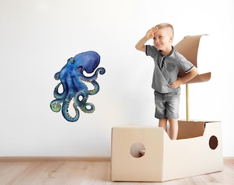 Op de afbeelding: Een blauwe en groene octopus wanddecoratie met een kind dat speelt in een kartonnen doos in de vorm van een boot.