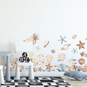 May include: A white wall with a variety of brown and beige seashells and starfish decals. The decals are arranged in a wave-like pattern. There is a small wooden chair and a table in the foreground.
