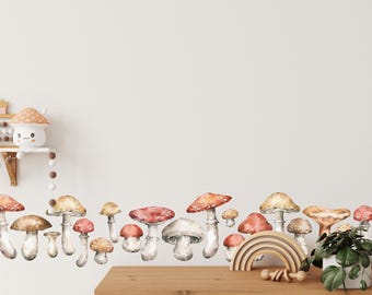 May include: Watercolor mushroom wall decals in various sizes and colors, including red, brown, and tan. The mushrooms are arranged in a horizontal line, creating a whimsical border. A wooden rainbow and a small potted plant are on a wooden cabinet.