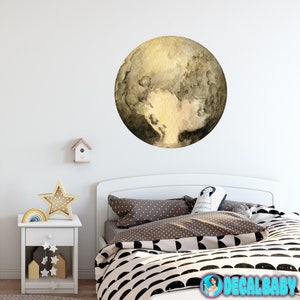 May include: A watercolor-style wall decal of Pluto, a dwarf planet in our solar system. The decal is a light brown color with darker brown markings. It is shown on a white wall above a white bed with black and white bedding.