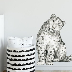 May include: A watercolor-style snow leopard wall decal in black and white. The leopard is sitting with its tail curled around its body. The decal is perfect for adding a touch of whimsy to any room.