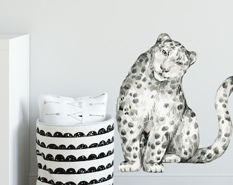 May include: A watercolor-style snow leopard wall decal in black and white. The leopard is sitting with its tail curled around its body. The decal is perfect for adding a touch of whimsy to any room.