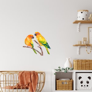 May include: Two yellow and orange parrots with green wings perched on a branch. The parrots are facing each other and have their beaks open.