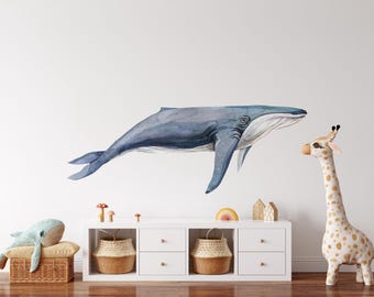 May include: A watercolor illustration of a blue whale with a giraffe plush toy in the background. The whale is swimming to the left and the giraffe is standing on a white surface. There are also some small decorative items on a white shelf.