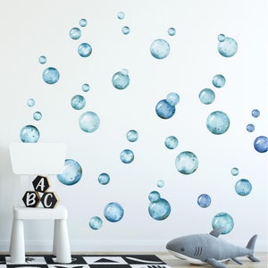 May include: A white wall with blue watercolor bubble decals. The decals are various sizes and are scattered across the wall. There is a white stool with wooden blocks that spell "ABC" in front of the wall.