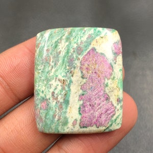 Peut inclure: Une pierre précieuse carrée de couleur verte et rose avec des veines blanches et brunes. La pierre précieuse a une surface lisse et polie.