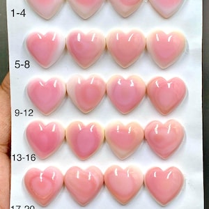 May include: A collection of 20 smooth, heart-shaped cabochons arranged in five rows of four on a white card. Each piece features a gradient of soft pink and white tones. The card is labeled with numbers 1-20, a size of 15mm, and a count of 20pcs.