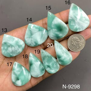 May include: A collection of eight polished, teardrop-shaped green and white marbled cabochons labeled with numbers 13 through 20. A United States quarter coin is included for scale, providing a clear reference for the size of these smooth gemstones.