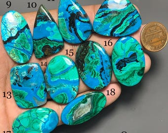 Puede incluir: Una colección de diez cabujones pulidos de crisocola y malaquita en varias formas, numerados del 9 al 18, con patrones vibrantes en azul y verde con vetas negras. Se incluye una moneda de un centavo de cobre para escala, y el texto Q-1400.