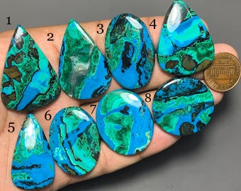 Puede incluir: Ocho cabujones de crisocola pulidos con patrones vibrantes en azul y verde, numerados del uno al ocho, mostrados junto a una moneda de cobre para comparar el tamaño. Las piedras presentan remolinos orgánicos en turquesa, cerceta y marrón.