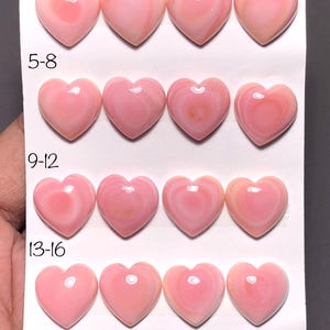 Peut inclure: Seize pierres précieuses roses polies en forme de cœur, disposées en quatre rangées de quatre. Les pierres ont une finition brillante et varient légèrement en teinte, allant du pâle au rose plus foncé. La carte indique "1-4", "5-8", "9-12", "13-16", "(6mm" et "16pcs".