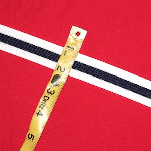 May include: A white and black striped ribbon with a yellow measuring tape on top. The tape measures 5 inches.