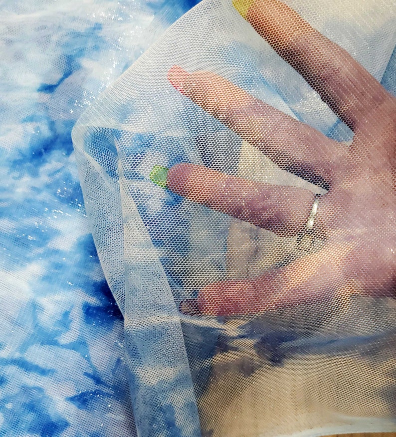 May include: A sheer white tulle fabric with a fine mesh pattern. The fabric is draped over a blue and white tie-dye fabric.