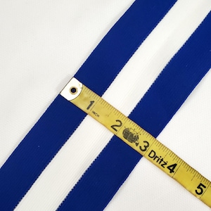 May include: Close-up of white fabric with two blue stripes. A measuring tape reads "1 inch, 2, 3 Dritz 4, 5".