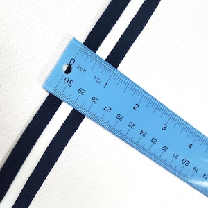 May include: Close-up of a white fabric with two black stripes. A blue ruler is placed on top of the fabric, showing the stripes are 1.27 cm wide.