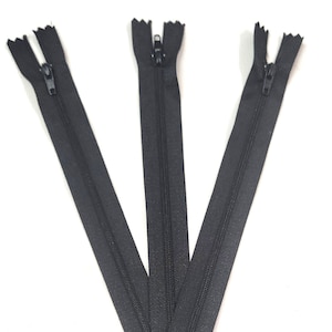 May include: Three black zipper closures, each with a metal slider. The zippers are laid out in a V shape.
