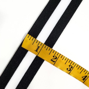 Puede incluir: Cinta rayada en blanco y negro con una cinta métrica amarilla que muestra de 1 a 4 pulgadas.