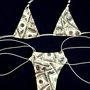 Könnte beinhalten: Ein weißer Bikini mit Geld-Print. Das Bikinioberteil ist im Dreieckstil und das Unterteil im frechen Stil. Der Bikini ist aus weichem, dehnbarem Stoff.