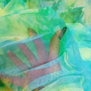 以下が含まれることがあります： 手は、透き通ったカラフルな布地を通して伸びています。布地は、黄色、緑、青のグラデーションになっています。